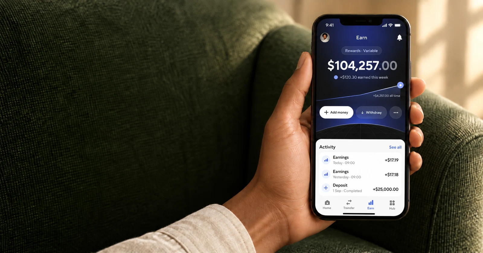 A person holding a phone showing a funded Dara Earn account, with an Earn balance of $104,257.00 and earnings this week of $120.30, beside a green woven armchair.